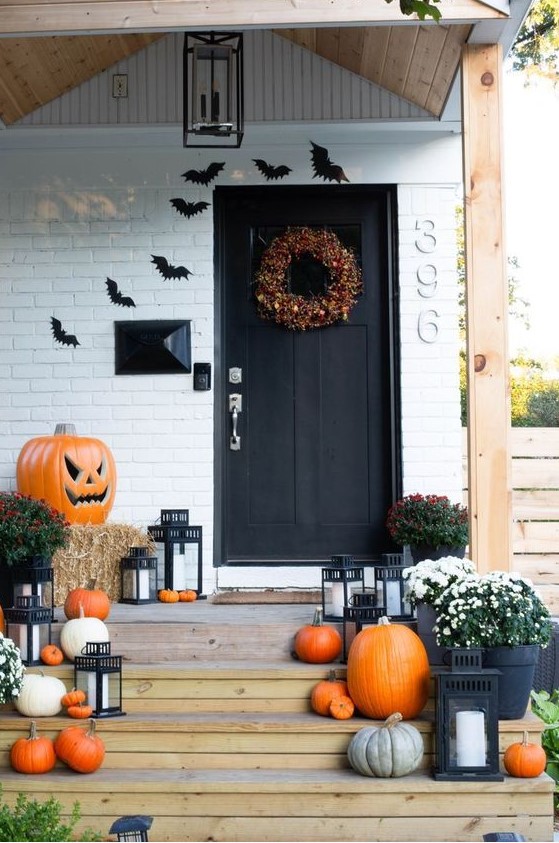 a classic front porch with bats, lots of bright pumpkins, hat, candle lanterns and a bold fall wreath