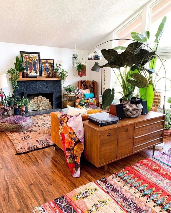 a colorful boho living room with a fireplace, a mustard sofa, bright rugs and pillows, potted plants and bold artwork