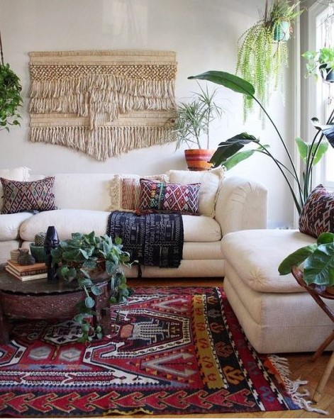 a colorful boho living space with a macrame hanging, a boho rug and pillows, potted greenery and neutral furniture
