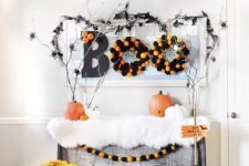 a console table styled for Halloween in a bold and fun way, with black witches’ hats, faux fur, pumpkins, wreaths and bold blooms, branches and spiders