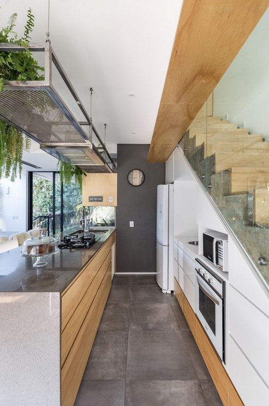 A contemporary white kitchen with sleek built in storage units in the staircase, a large kitchen island, a metal shelf with greenery