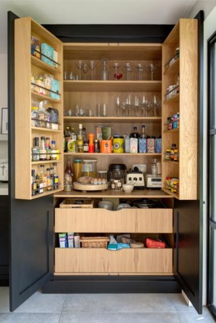 a contrasting pantry with black panels, stained shelves and drawers, wine glasses, drinks, spices, oils and various food in drawers