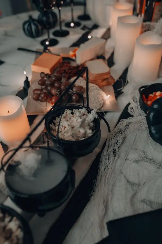 a cool Halloween table with cauldrons used to serve various sweets like popcorn is a very fresh and stylish idea for Halloween