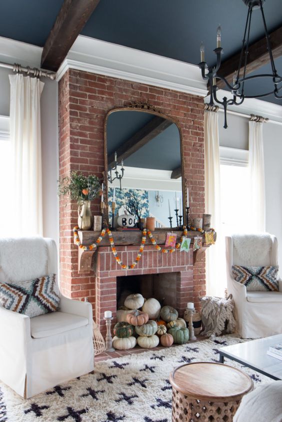 a cozy living room with a black ceiling, white seating furniture, a coffee table, a red brick fireplace with lovely autumnal decor