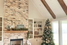 a cozy living room with a large brick clad fireplace, built-in shelves, some seating furniture and a Christmas tree