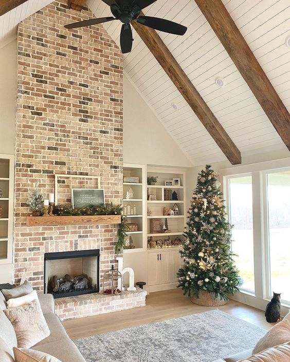 a cozy living room with a large brick clad fireplace, built-in shelves, some seating furniture and a Christmas tree