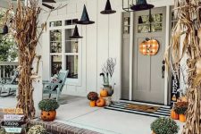 a cozy rustic Halloween porch with dried corn husks, pumpkins, pumpkin planters with blooms and witches’ hats