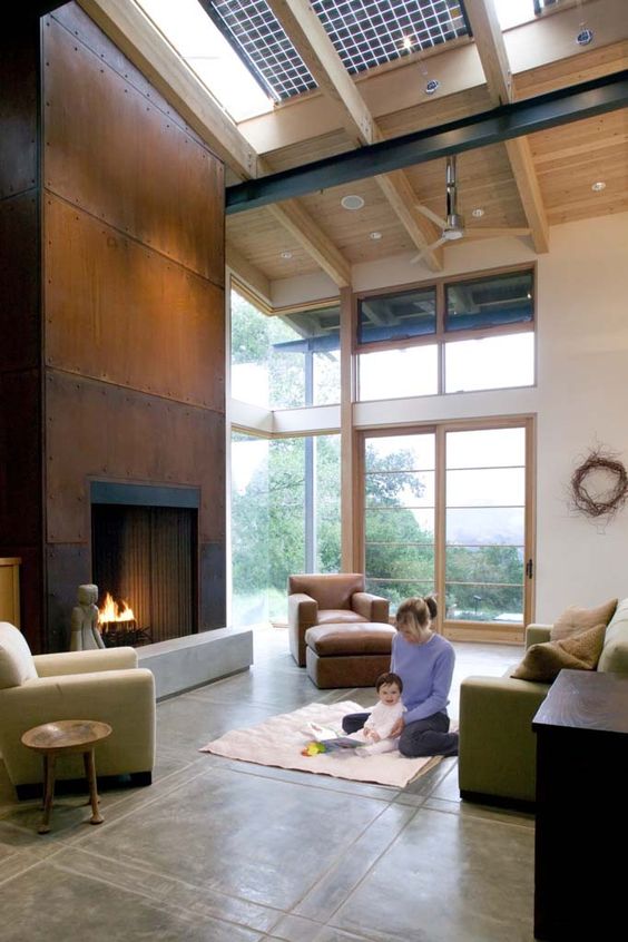 A double height living room with a copper clad fireplace, green seating furniture, a tan chair and some lights
