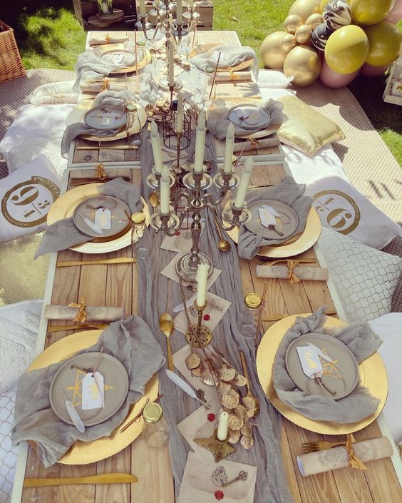 a grey and gold Halloween party tablescape with grey linens, tall and thin candles, gold leaves and Harry Potter signs