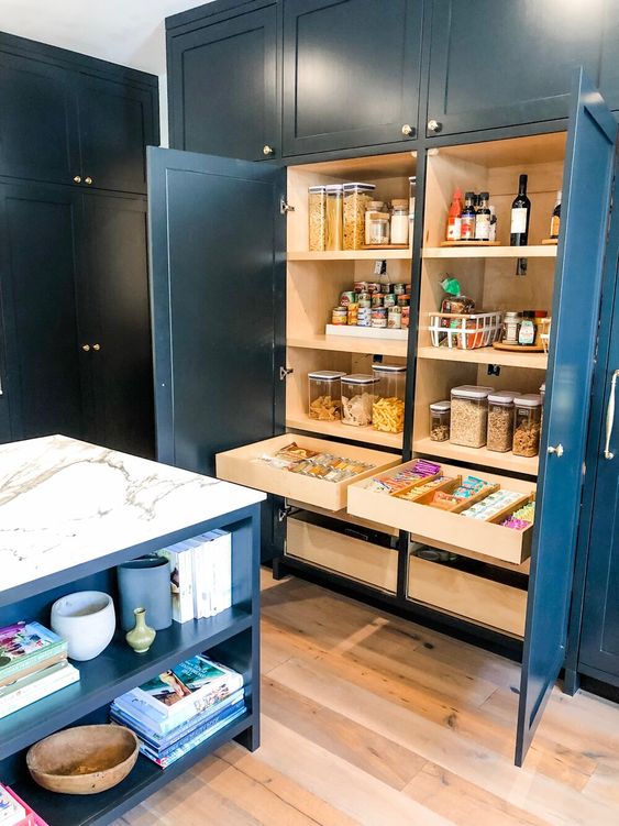 A large built in pantry with open shelves that store food in jars, oils and spices, drawers with food and cookies