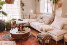 a lovely neutral boho living room with a creamy sofa, a bold printed rug, a coffee table, potted greenery and pillows