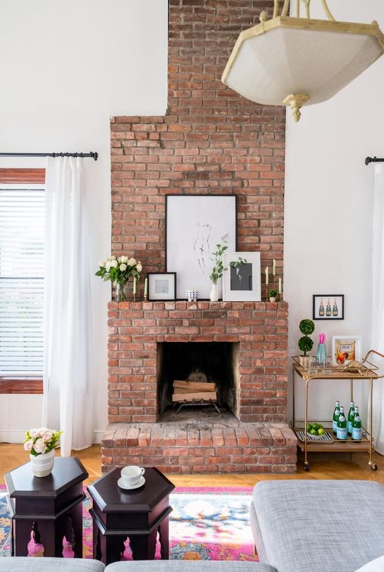 a lovely red brick fireplace with a matching mantel, artworks, candles and blooms and greenery is a chic addition to the space