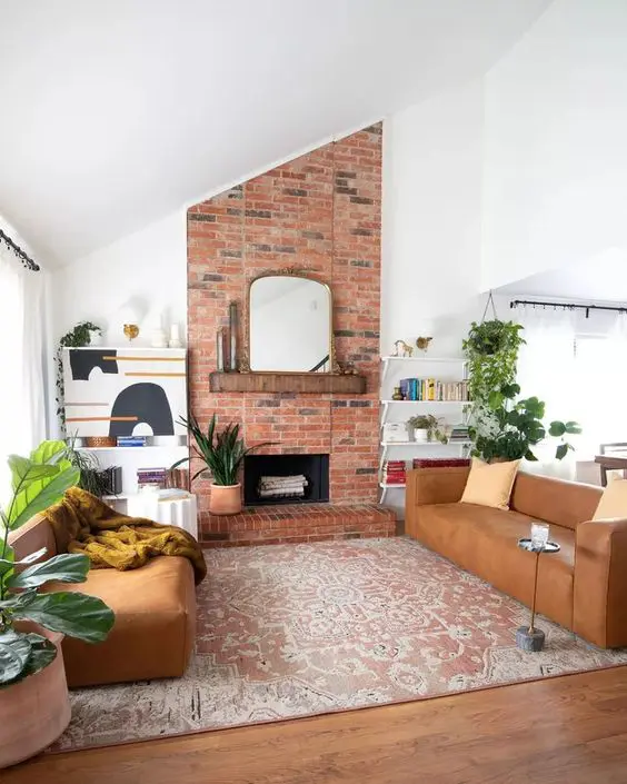 A mid century modern living room with a red brick fireplace, amber leather sofas, greenery and open shelves