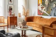 a modern and boho living room with a rust-colored sofa, rattan chairs, wooden and leather furniture and a statement artwork