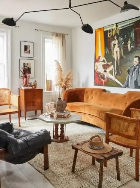 A modern and boho living room with a rust colored sofa, rattan chairs, wooden and leather furniture and a statement artwork