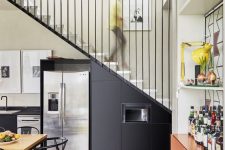 a modern black kitchen with metal cabinets integrated under the stairs, with built-in appliances and black chairs is a cool idea