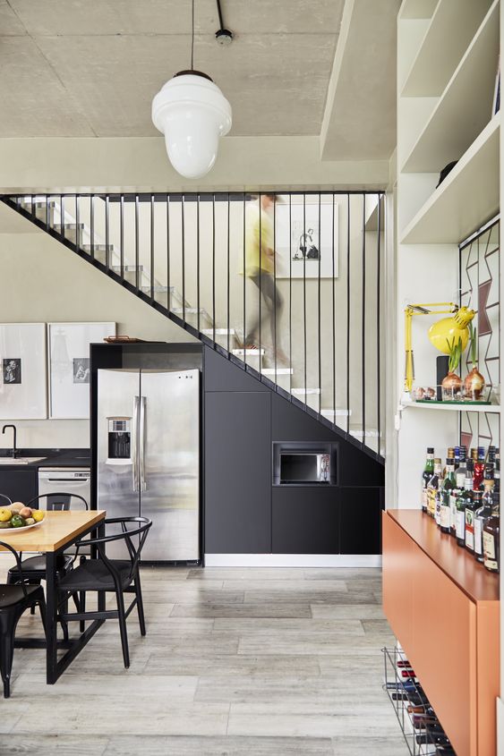 A modern black kitchen with metal cabinets integrated under the stairs, with built in appliances and black chairs is a cool idea