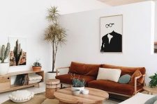 a modern boho living room with a burnt orange sofa and a neutral chair, a coffee table, a credenza, some art and plants