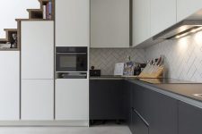 a modern graphite grey and white kitchen with slek cabinets, a herringbone tile backsplash and built-in lights