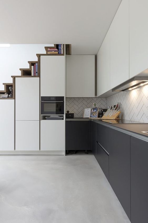 A modern graphite grey and white kitchen with slek cabinets, a herringbone tile backsplash and built in lights