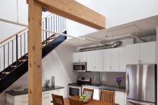 a modern kitchen with white cabinets and black countertops placed under the stairs, with a dining set of stained wood
