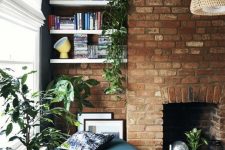 a modern living room with a red brick accent wall with a fireplace, niche shelves, potted greenery, a cozy blue ottoman