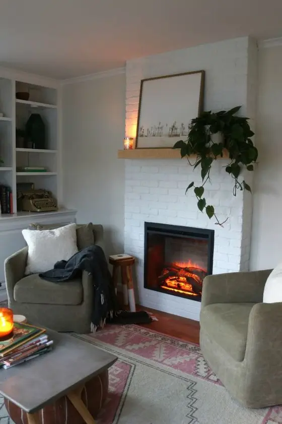 a modern neutral living room with a whitewashed brick fireplace, green chairs, a mantel with potted greenery is welcoming