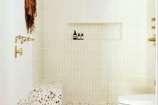 a neutral bathroom with skinny tiles and a bright terrazzo floor, a shower space, a toilet and some gold fixtures