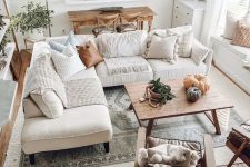 a neutral boho farmhouse living room with a white corner sofa, a wooden table, leather chairs, potted greenery and pumpkins