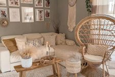 a neutral boho living room with grey walls, a neutral sectional and macrame pillows, a papasan chair, layered rugs and a bench