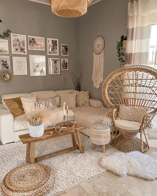 a neutral boho living room with grey walls, a neutral sectional and macrame pillows, a papasan chair, layered rugs and a bench