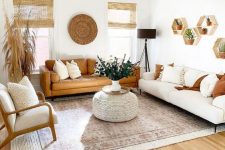 a neutral boho living room with with a white and an amber sofa, a chair, a woven pouf, some greenery, hexagon shelves and grasses