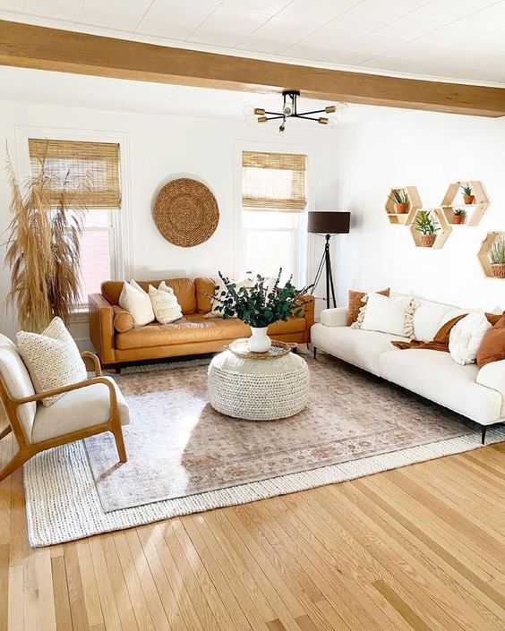 a neutral boho living room with with a white and an amber sofa, a chair, a woven pouf, some greenery, hexagon shelves and grasses