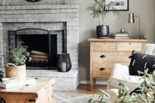 a neutral farmhouse living room with a whitewashed brick fireplace, wooden and neutral upholstered furniture and potted plants