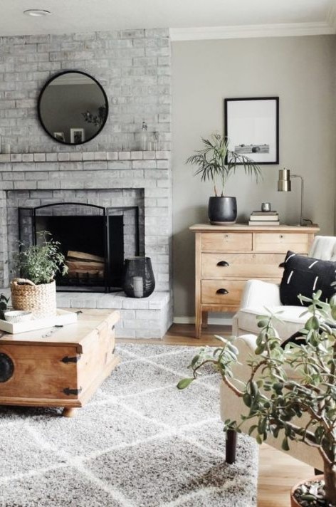 a neutral farmhouse living room with a whitewashed brick fireplace, wooden and neutral upholstered furniture and potted plants