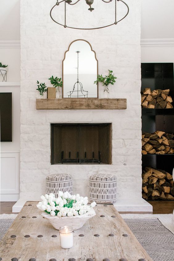 a neutral farmhouse living room with firewood storage, a white brick fireplace, a whitewashed table and a chandelier