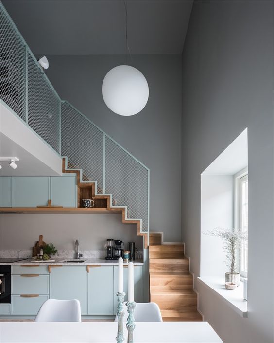 a pale blue Scandinavian kitchen placed under the stairs, with stained touches and greenery is a lovely space