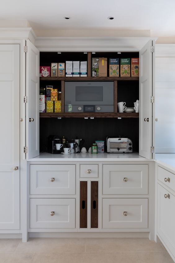 a pantry built into kitchen cabinetry, with a black backdrop, stained shelves, some food, a coffee machine and a toaster as a breakfast station