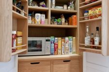 a pantry with stained shelves, drawers, baskets and a microwave and various spiaces and oils plus some food