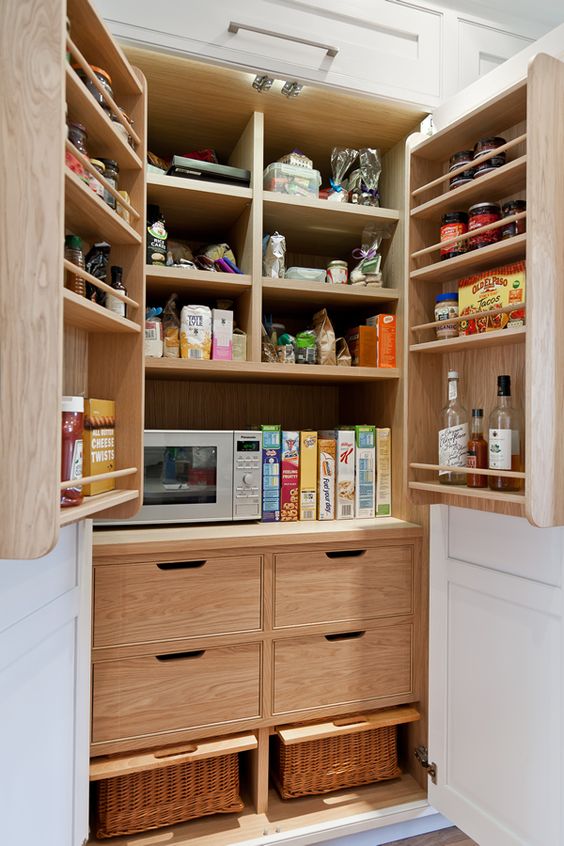 a pantry with stained shelves, drawers, baskets and a microwave and various spiaces and oils plus some food