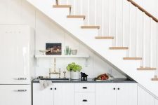a pretty farmhouse under the stairs kitchenette with planked cabients, black countertops, a fridge and a shelf is cool