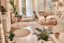 a pretty neutral boho living room with a sectional, a lot of macrame pillows, white storage furniture, woven pendant lamps and potted plants