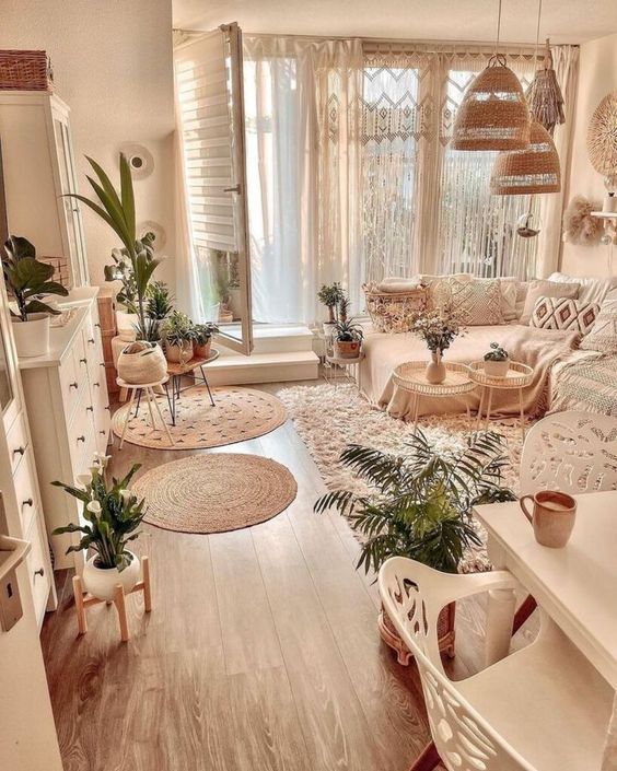 a pretty neutral boho living room with a sectional, a lot of macrame pillows, white storage furniture, woven pendant lamps and potted plants