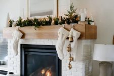 a pretty white brick fireplace with a mantel styled for Christmas, with stockings, bells, evergreens and lights