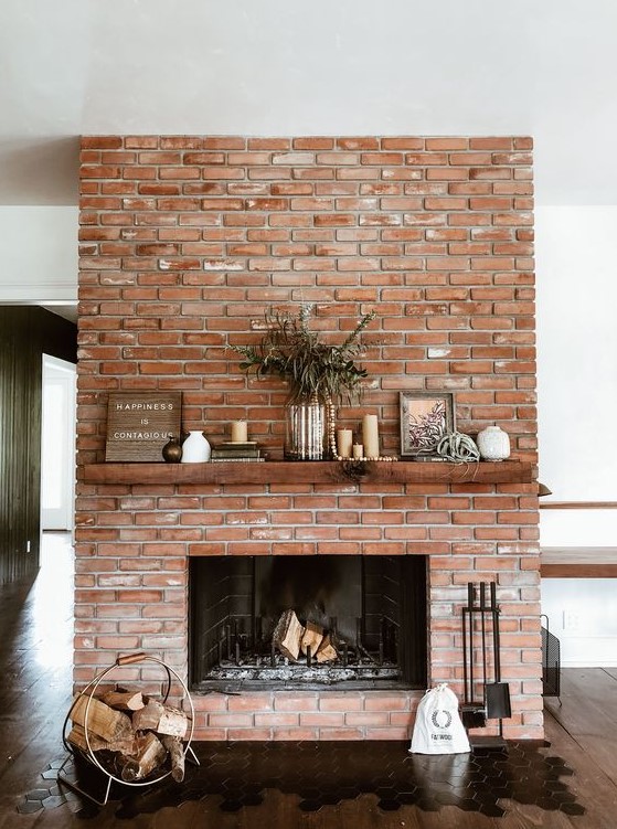 A red brick fireplace with a rich stained mantel, a modern and chic firewood stand, lovely decor on the mantel is cool