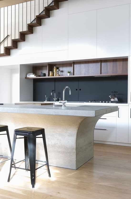 a refined contemporary kitchen with sleek cabinets built in under the stairs, with a black backsplash, a catchy kitchen island