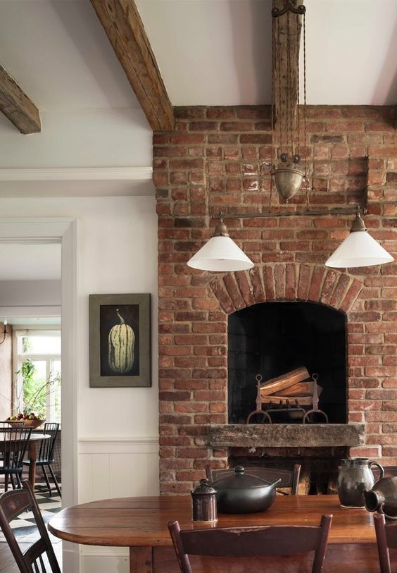 a refined vintage dining room with a red brick fireplace, dark stained furniture, wooden beams and cool lamps