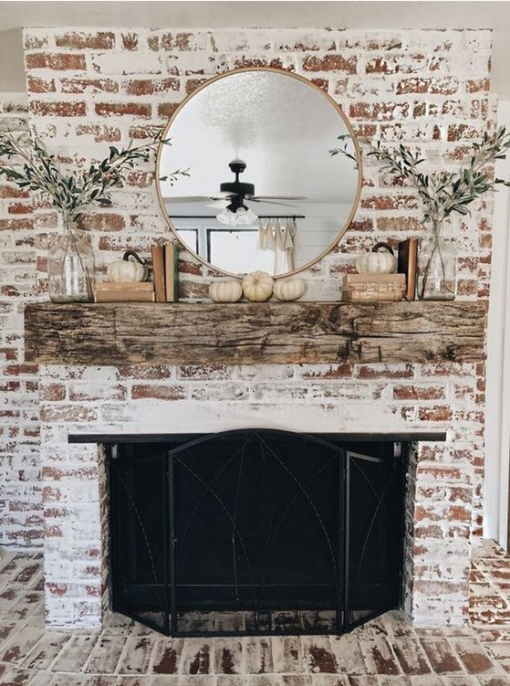 a rustic and shabby chic whitewashed brick fireplace with a weathered wood mantel, a beautiful metal screen, greenery and pumpkins for the fall