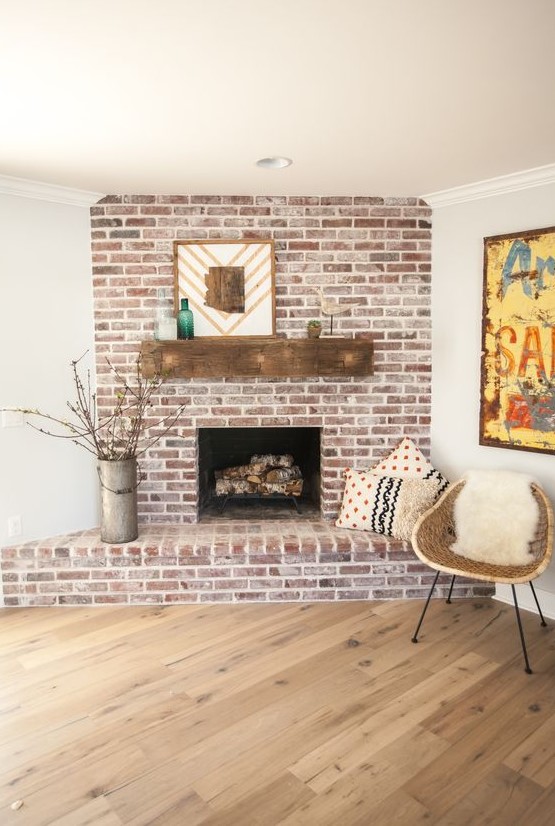 A rustic whitewashed red brick fireplace with a wooden mantel, mid century modern decor and printed pillows