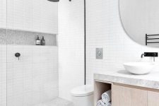 a serene bathroom clad with skinny white tiles, grey terrazzo ones on the floor and a floating vanity and a round mirror